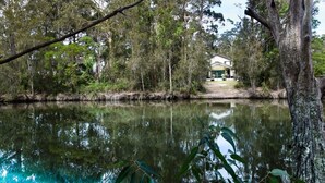 A house by a calm lake surrounded by dense trees. - Relax at the Park by Book Jervis Bay (Sanctuary Point)