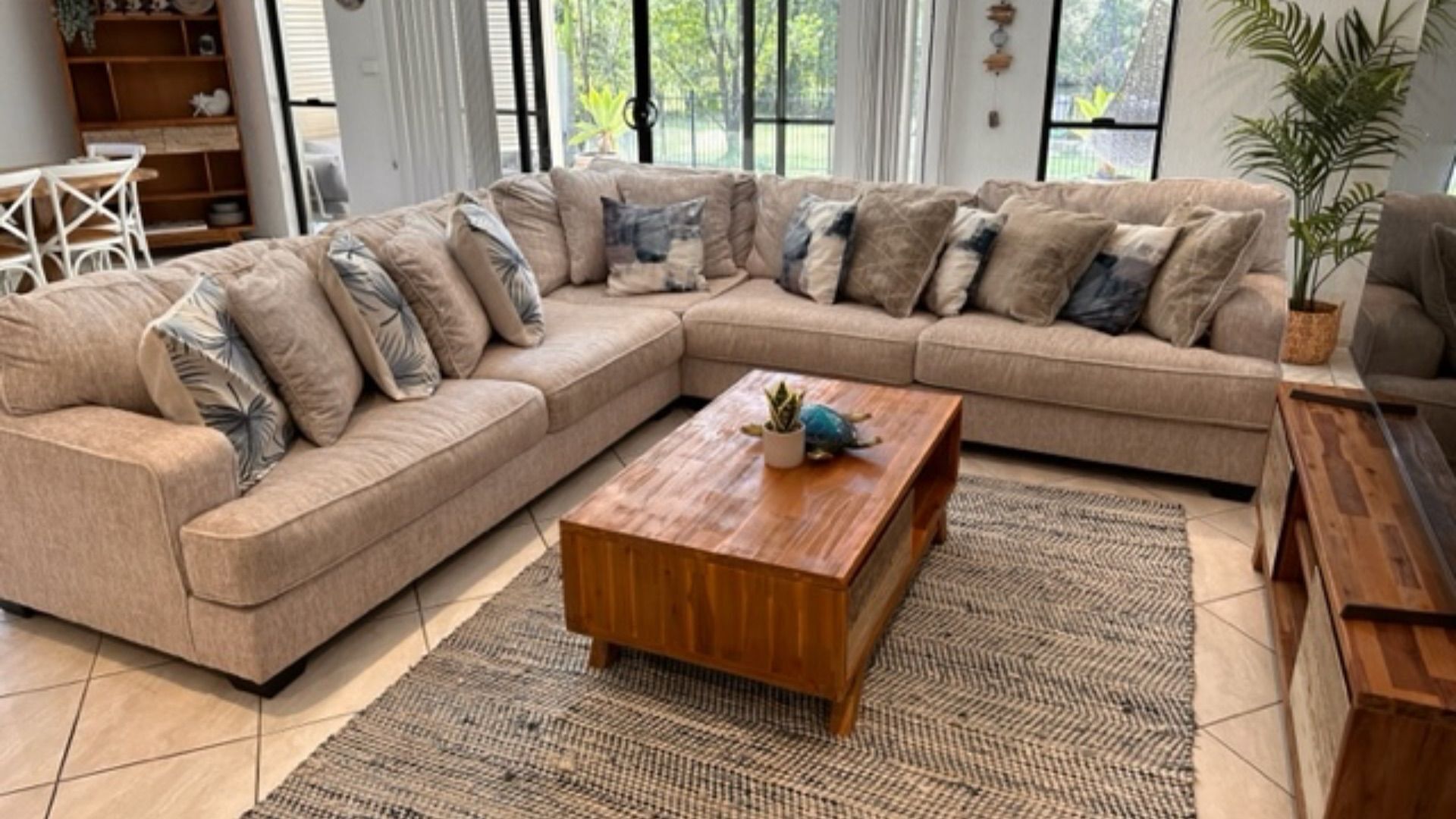 A modern living room with a beige sectional sofa, a wooden coffee table, and a patterned rug.