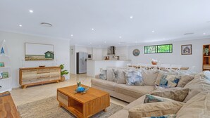 A spacious living room with a sofa, coffee table, and a dining area with chairs. - Relax at the Park by Book Jervis Bay (Sanctuary Point)
