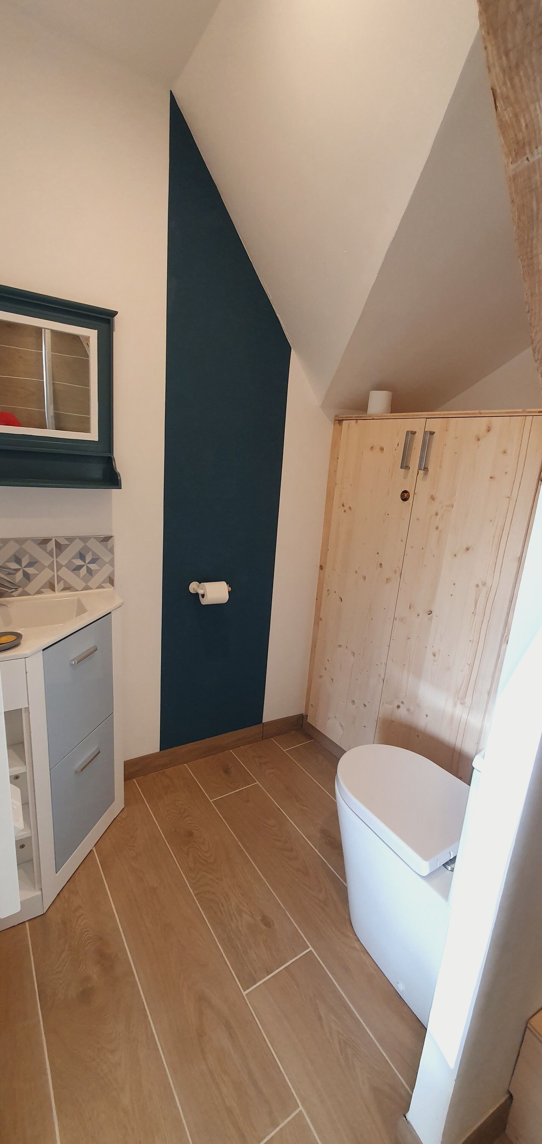 Une petite salle de bain aux dimensions réduites, avec des toilettes blanches, un meuble en bois et un sol carrelé.