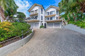 A modern two-story building with a central entrance, surrounded by lush greenery and palm trees.