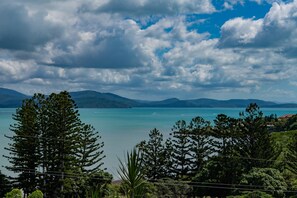 A coastal landscape with a clear view of the sea, distant mountains, and dense greenery.