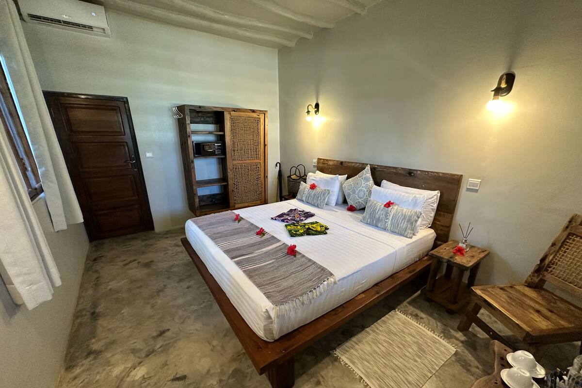 A bedroom with a bed, bedside tables, a wooden wardrobe, and a small table with a bottle.