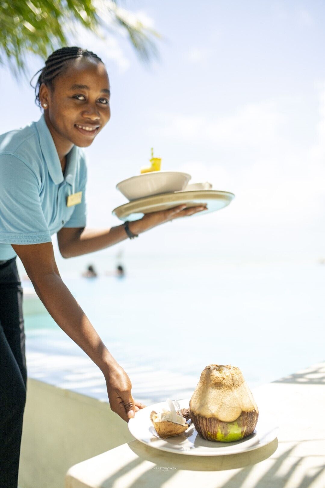 A person serving a coconut and a dessert on a plate by a poolside.