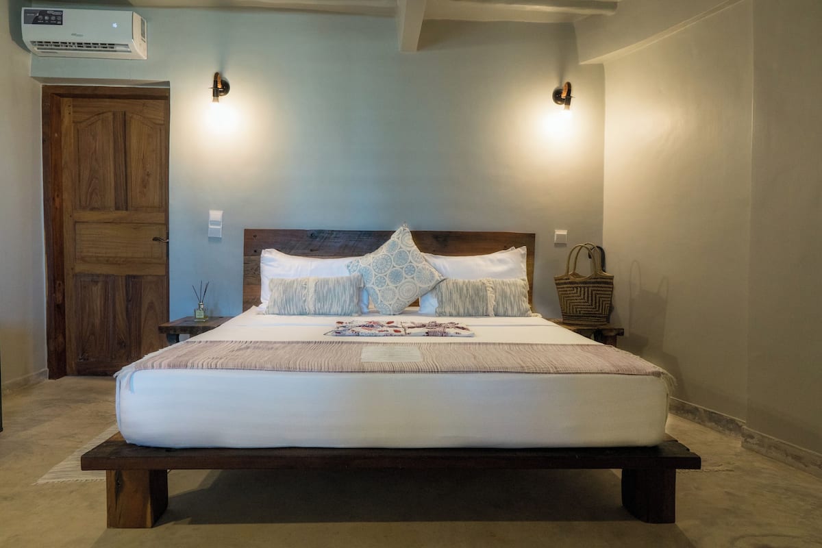 A bedroom with a wooden bed, two wall-mounted lights, a nightstand, and a wooden door.