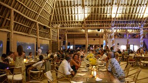 A spacious indoor dining area with bamboo ceiling and walls, wooden tables, and wicker chairs. - Ndame Paje Hotel (Paje)