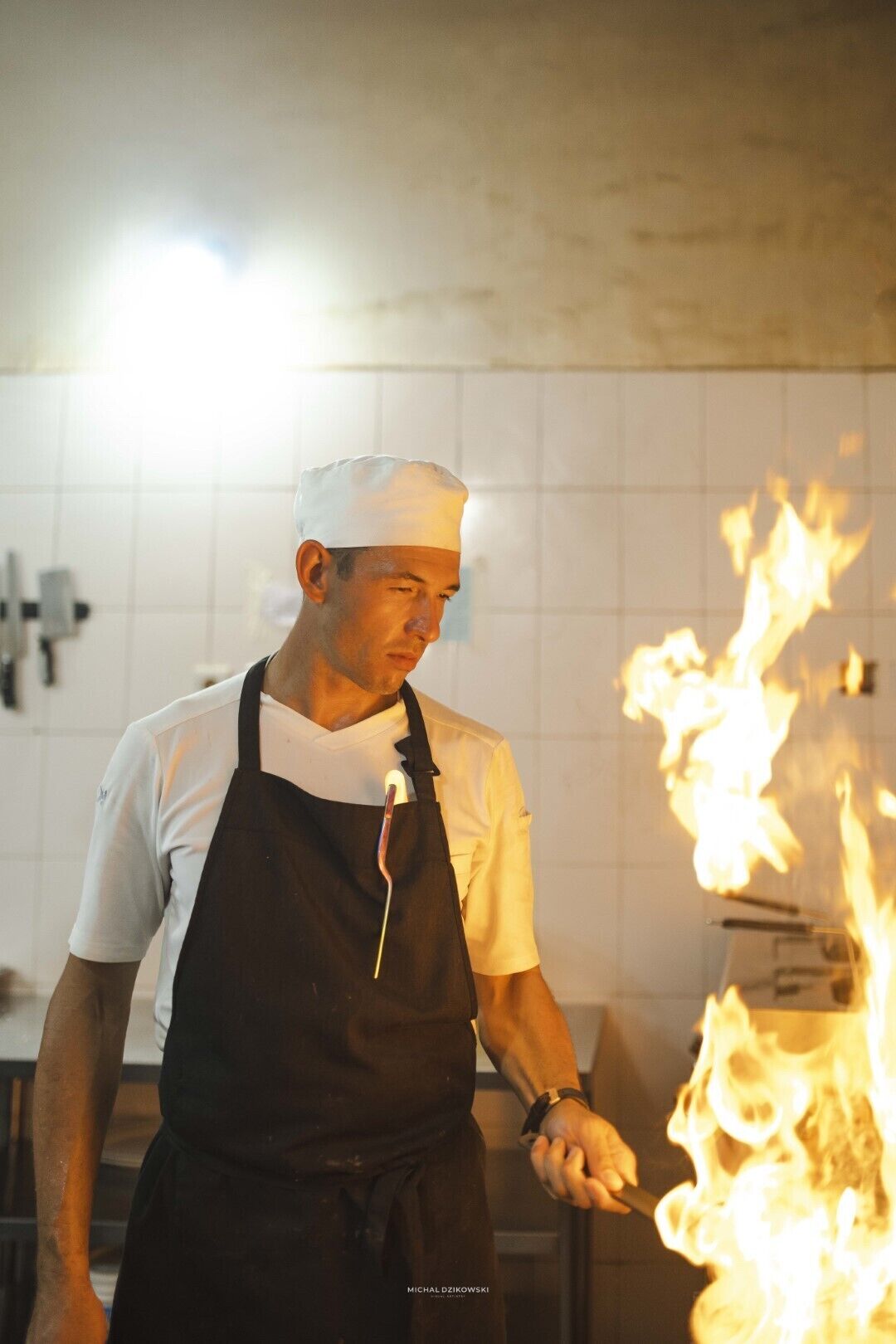 A chef performing a flambé with a torch in a kitchen.