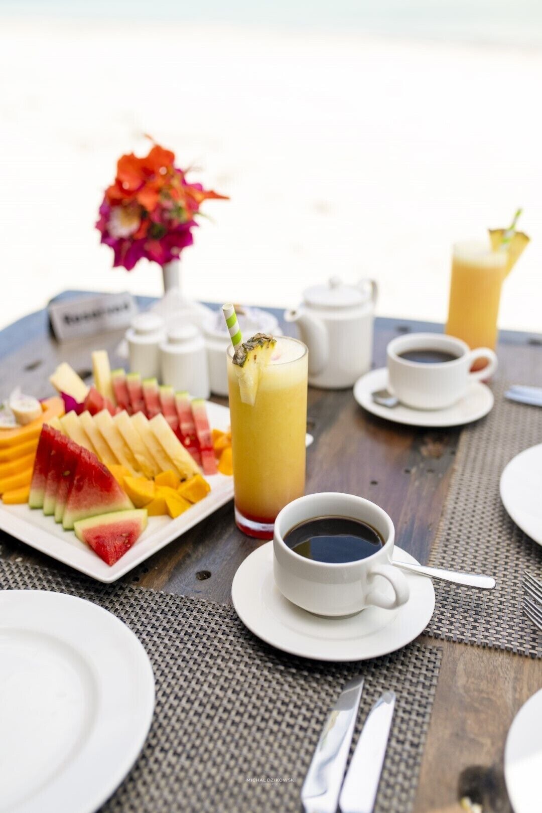 A breakfast setup with a fruit platter, a glass of juice, a cup of coffee, and a small vase with flowers.