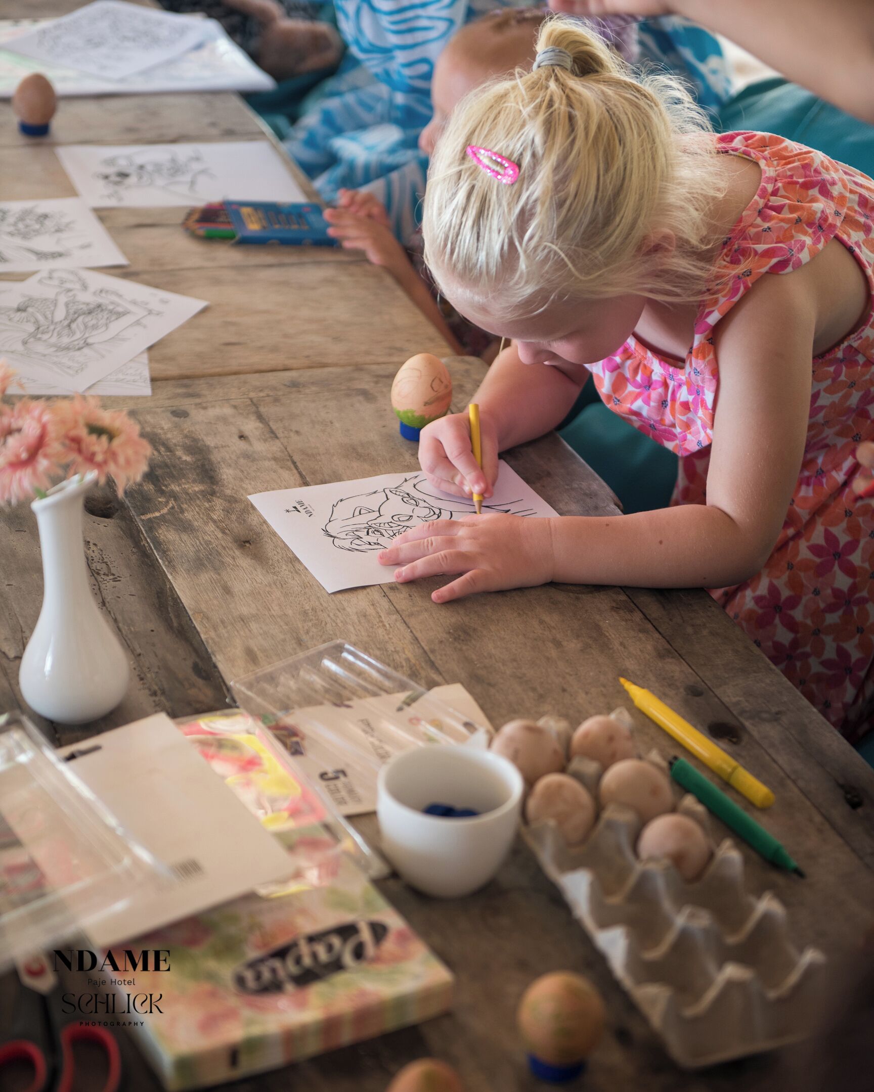 A child drawing on a paper at a wooden table with art supplies, including markers and crayons.