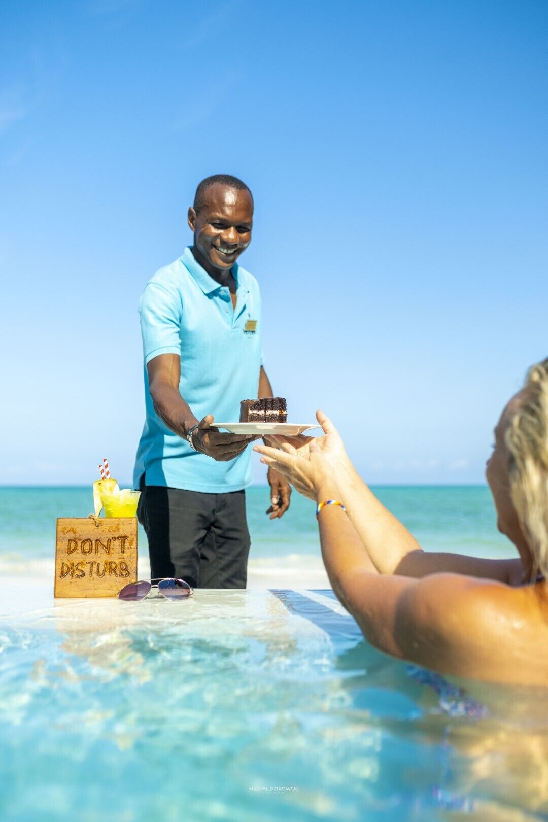 A person serving a dessert on a beach with a sign that reads "DON'T DISTURB".