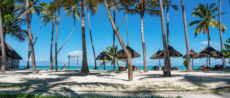A beach with palm trees, thatched umbrellas, and a clear blue sky.
