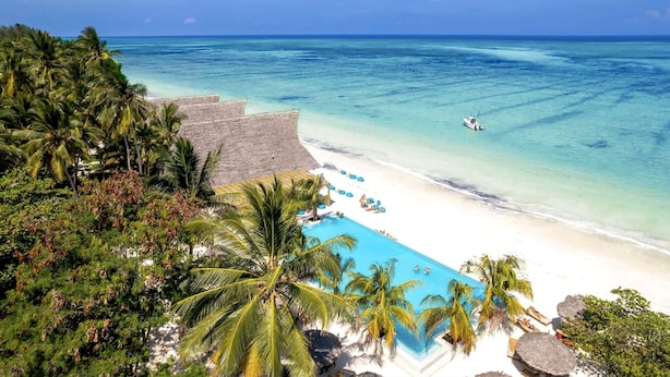 A beach resort with a swimming pool, palm trees, and a boat on the water. - Ndame Paje Hotel (Paje)