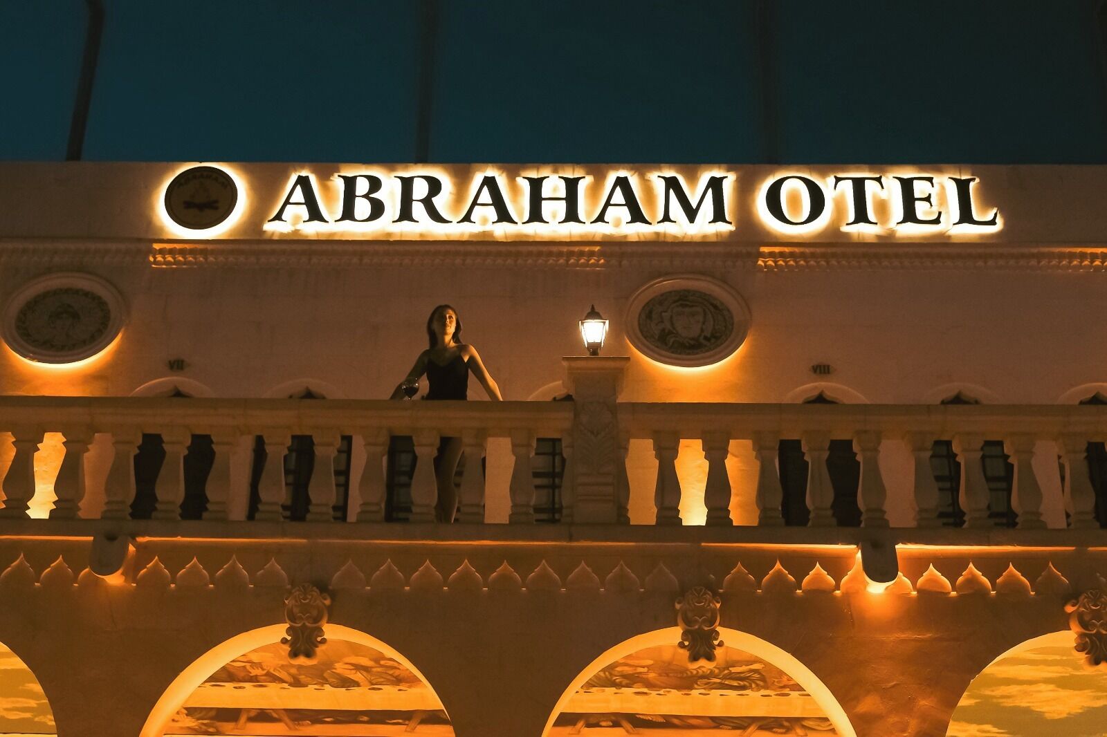 Exterior del Abraham Otel con un llamativo letrero iluminado, un balcón con una persona y un arco decorativo.