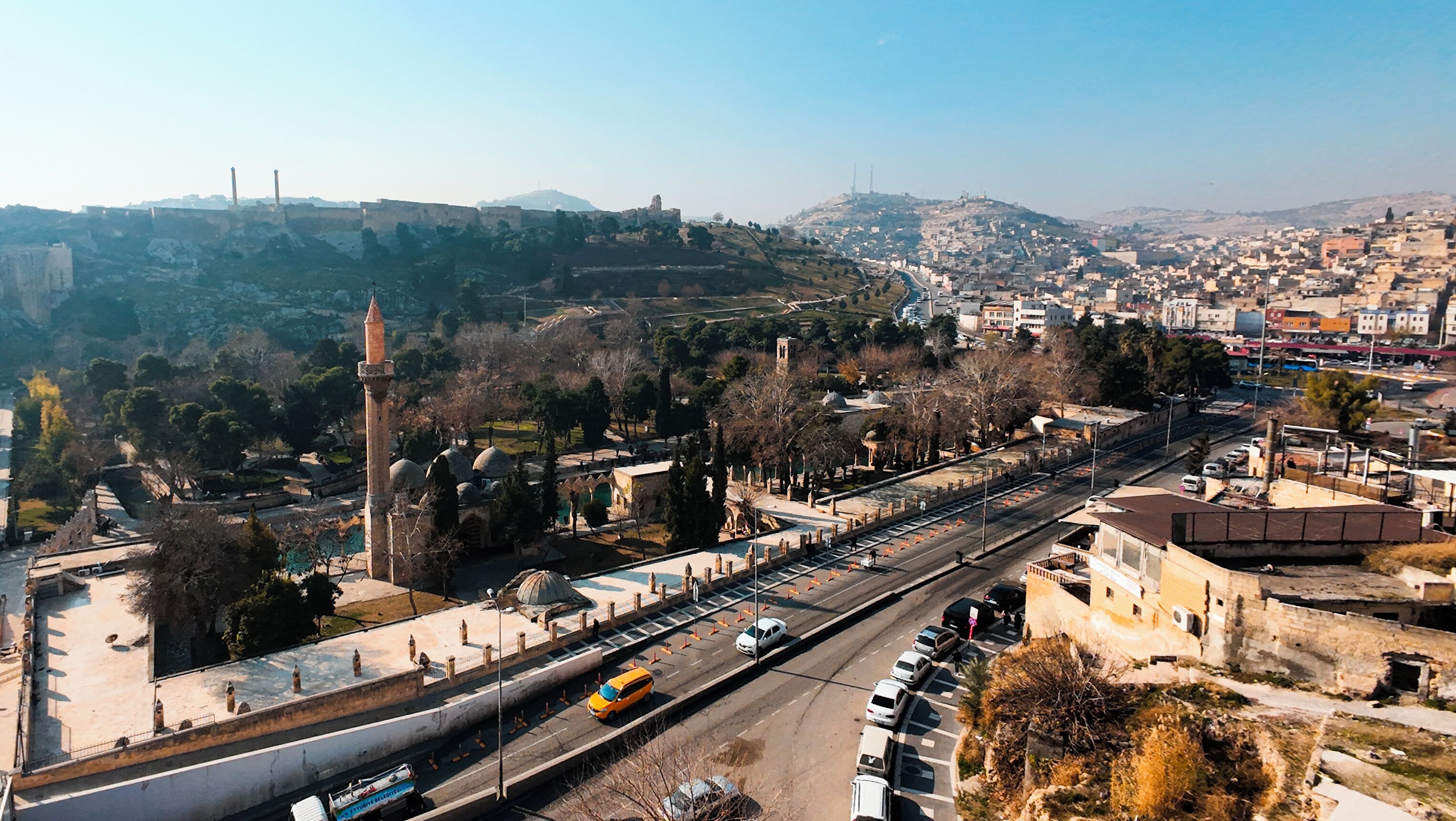 A cityscape with a prominent historical building featuring a tall minaret and domed structures, adjacent to a modern road with vehicles.