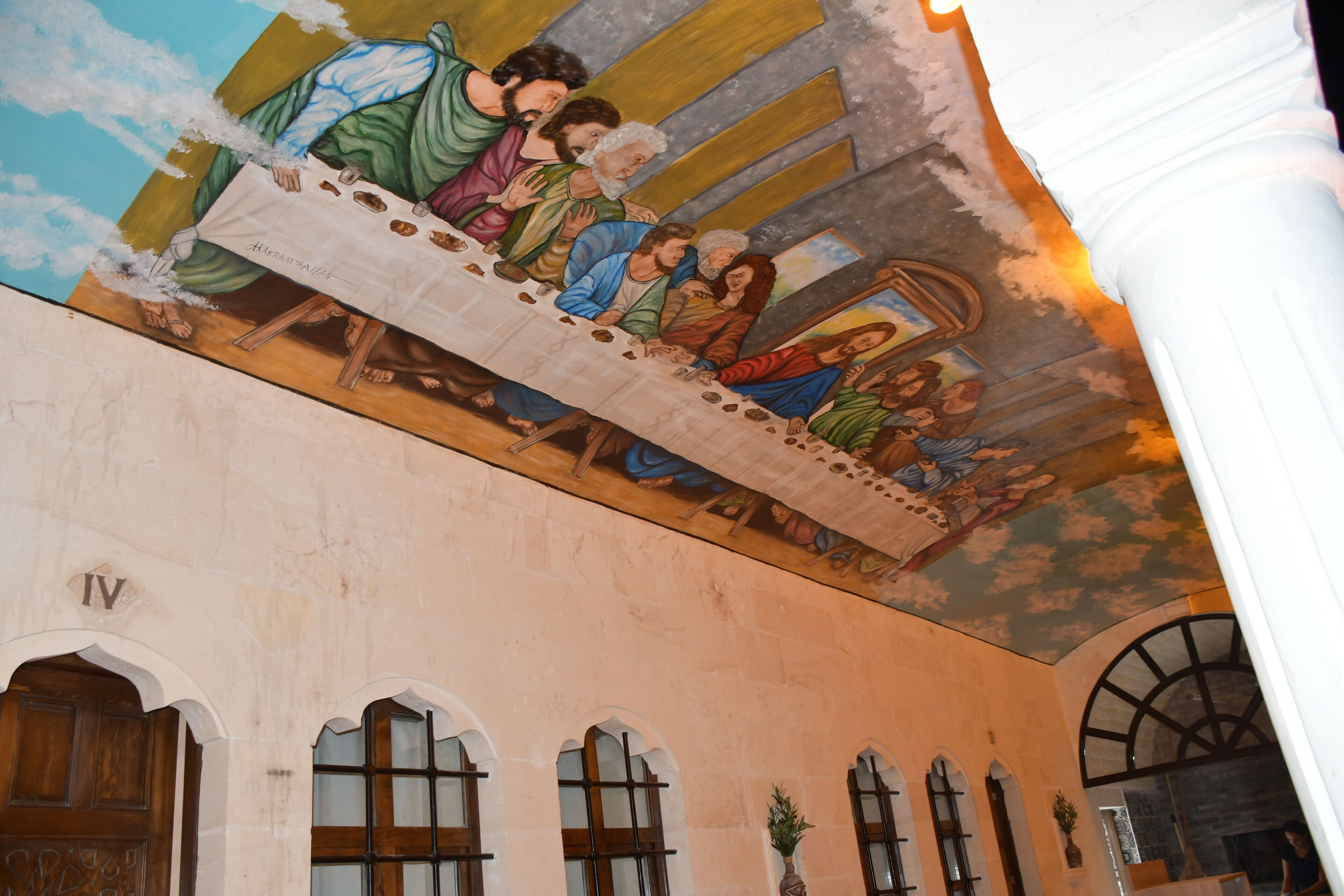 Une fresque murale représentant la Cène, peinte sur un plafond, des fenêtres en arc de cercle et une colonne.