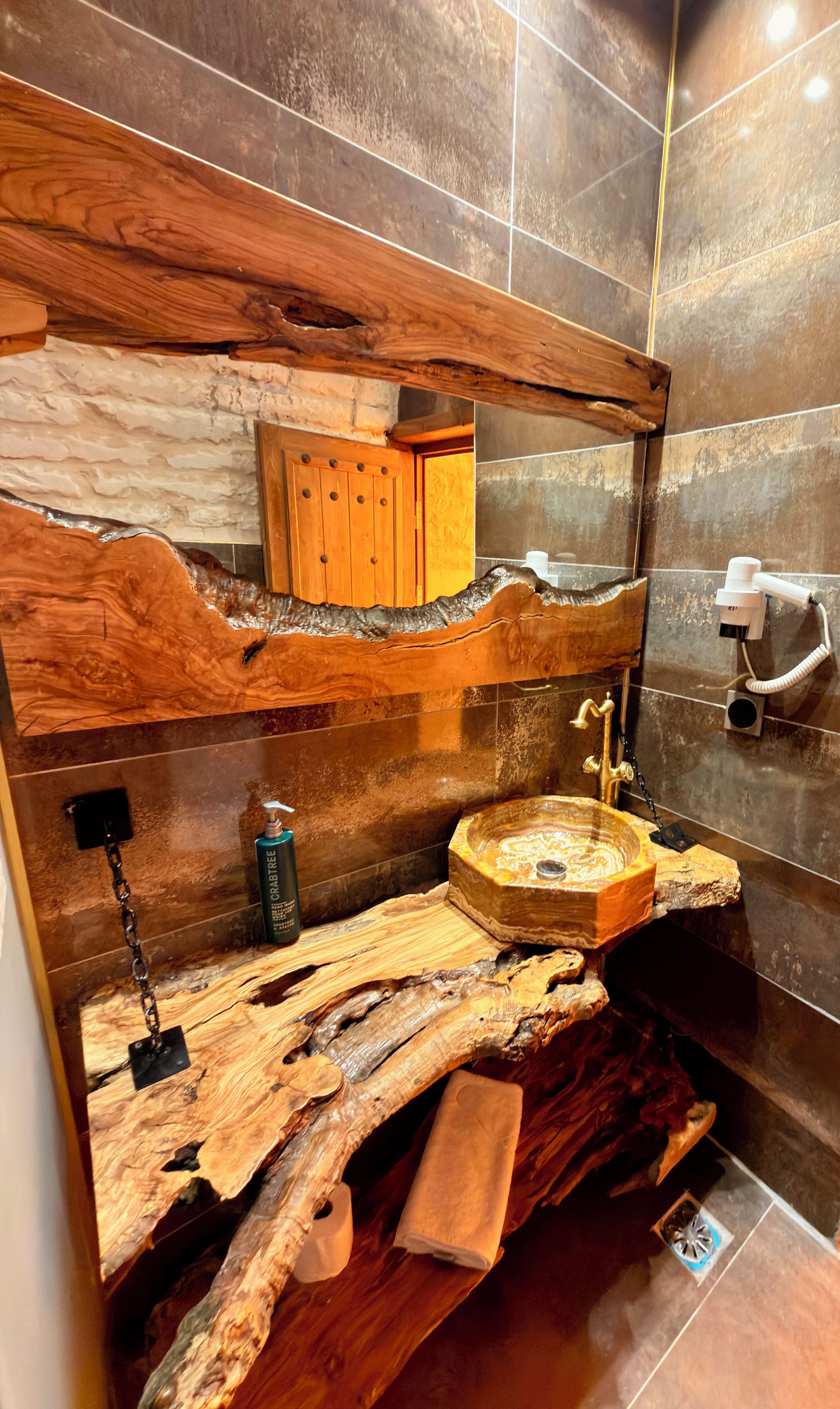 Une salle de bain avec un meuble-lavabo en bois, un évier doté d’un plan de travail imitant le marbre, et un miroir au-dessus.