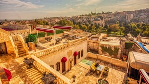 Eine Dachterrasse mit Außenbestuhlung, ein Gebäude mit steinernen Bögen und Blick auf eine historische Stadtlandschaft, darunter eine Moschee.