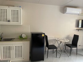 Cozinha compacta com pia, armários, geladeira preta, mesa pequena para dois e ar-condicionado fixado na parede.