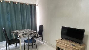 A dining area with a table covered by a newspaper tablecloth, two black chairs, and a television on a wooden stand. - Muangthong C3, C4 near Impact by Anna (Pak Kret)