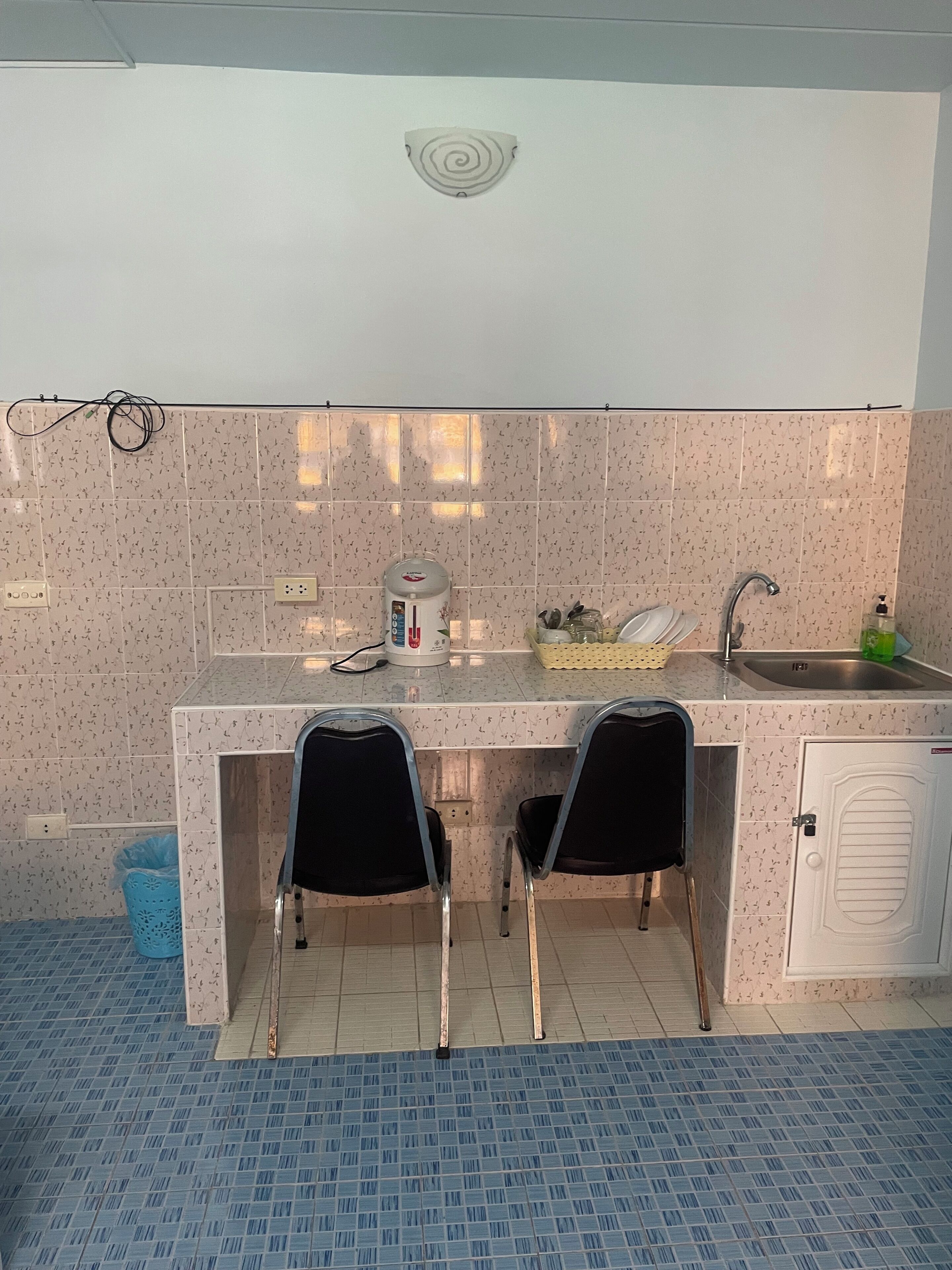 A kitchen with two black chairs, a sink, a kettle, and a cabinet.