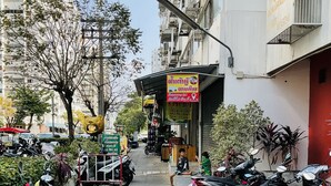 A street with parked motorcycles, a building with a sign, and a tree. - Muangthong C3, C4 near Impact by Anna (Pak Kret)