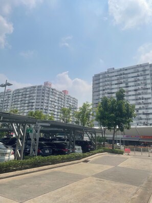 A parking structure with a fire exit sign, surrounded by trees and buildings in the background. - Muangthong C3, C4 near Impact by Anna (Pak Kret)