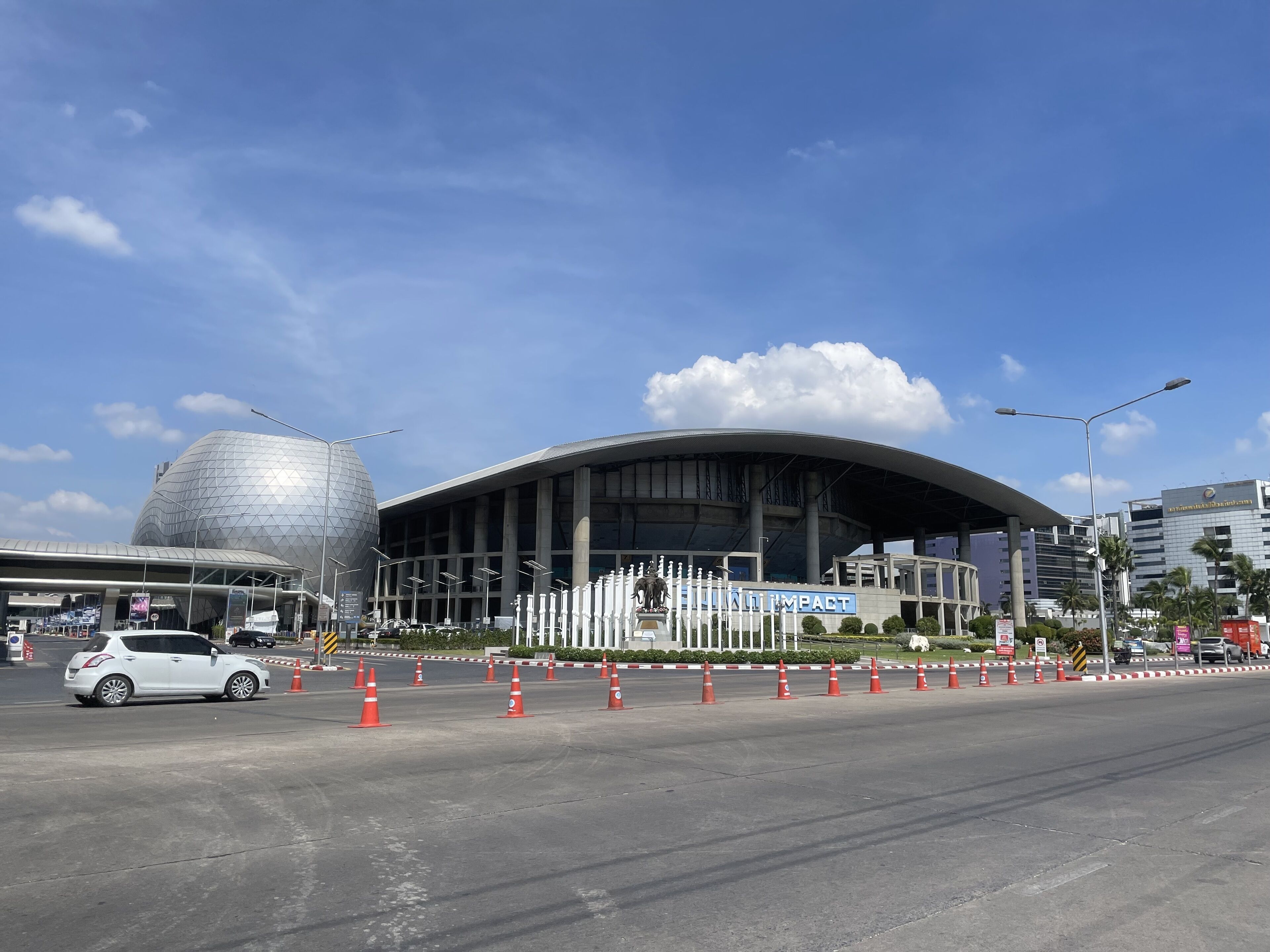 A modern building with a dome and a curved roof, surrounded by traffic cones and a white car.