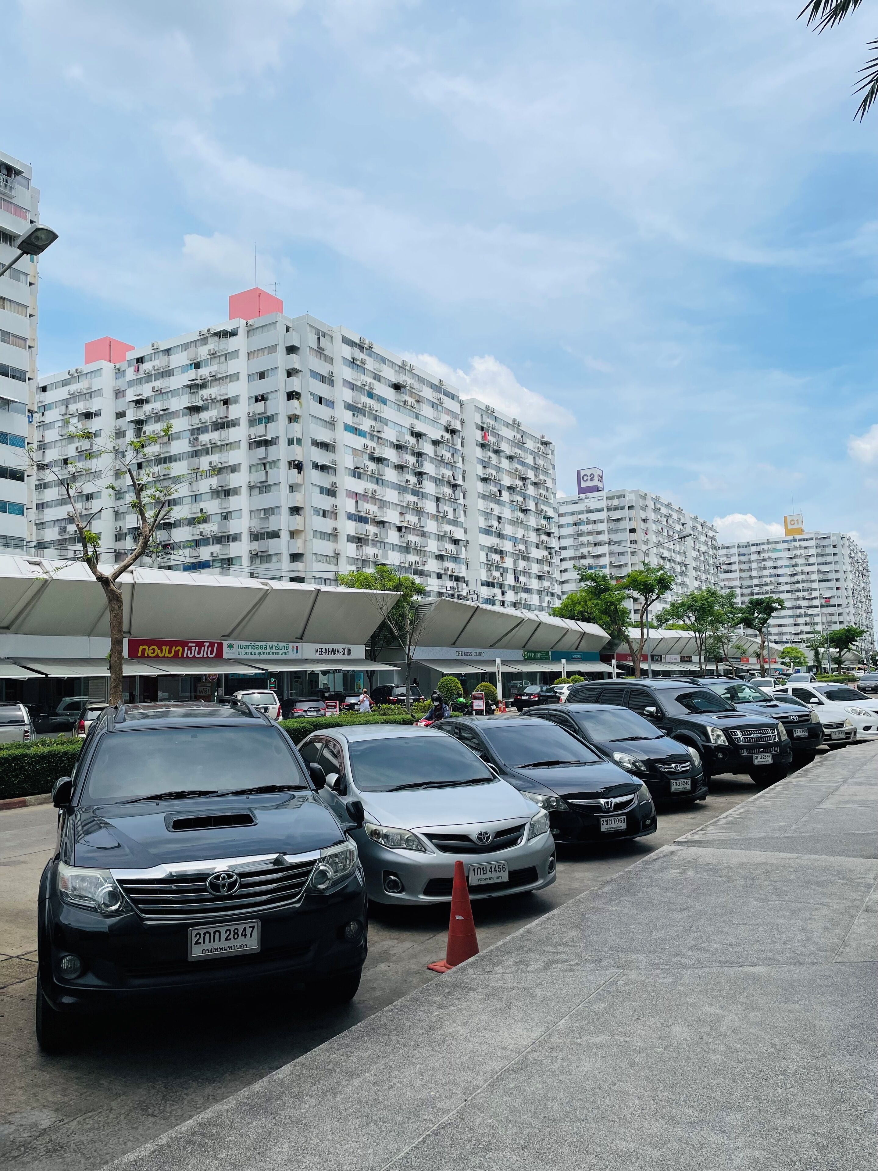 A parking lot with several cars, a building with multiple floors, and a sign with Thai text.