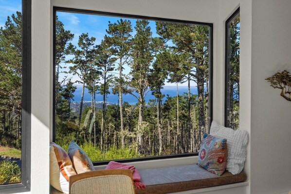 A room with a large window overlooking a forest and a body of water.