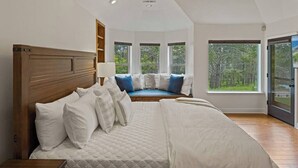 A bedroom with a large bed, a built-in bench with cushions, and large windows. - Pebble Beach's Los Altos (Pebble Beach)