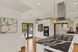 Une cuisine moderne avec des meubles blancs, un îlot central en marbre noir et des spots encastrés au plafond.