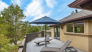 A deck with two lounge chairs and a large umbrella, overlooking a landscaped area with trees and a building in the background. - Pebble Beach's Los Altos (Pebble Beach)