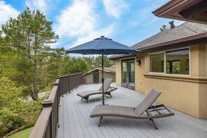 Una terrassa amb dues gandules i un parasol gran, amb vista a una zona enjardinada amb arbres i un edifici al fons.