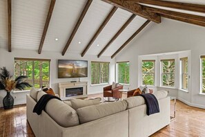 A spacious living room with a large sofa, a fireplace, and multiple windows offering views of the outdoors. - Pebble Beach's Los Altos (Pebble Beach)