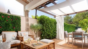 Une terrasse ensoleillée avec des meubles en bois, une table sur laquelle est posé un magazine et une plante en pot.