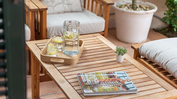 Une table en bois, un magazine, un pichet en verre contenant des tranches de citron et une petite plante en pot.