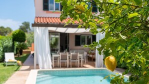 Une piscine avec un espace patio, un coin salon couvert et un citronnier au premier plan.