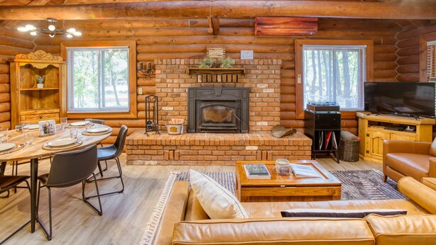 Interior de una cabaña de madera con chimenea, comedor y zona de estar.