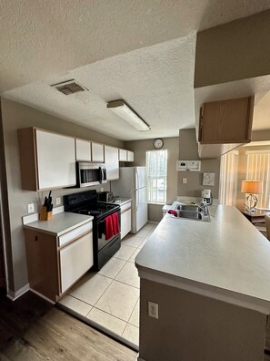 A kitchen with white cabinets, a black stove, a microwave, and a refrigerator.
