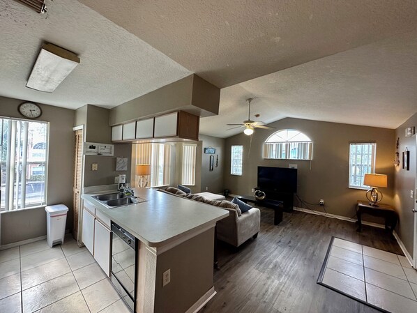 A spacious living area with a kitchen, a dining area, and a large window providing natural light.