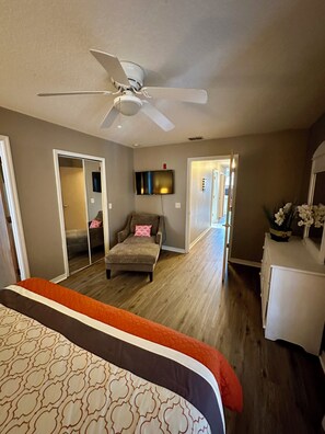 Ein Schlafzimmer mit Bett, Deckenventilator, Fernseher, Sessel und Kommode.
