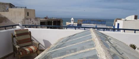 Terraço no telhado com vista para o mar, uma cadeira listrada e uma estrutura de estufa de vidro.