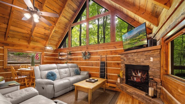 Ein rustikales Blockhaus-Interieur mit Kamin, Ledersofa, Esstisch aus Holz und einem an der Wand befestigten Fernseher.