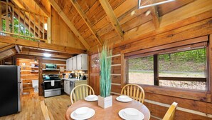 Ein Holzblockhaus-Interieur mit Essbereich, Küche und einem großen Fenster mit Blick auf einen Wald.