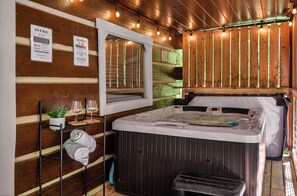 A wooden cabin interior with a hot tub, a shelf with towels, a potted plant, and a mirror.