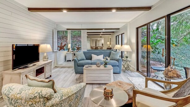 A modern living room with a sofa, coffee table, and TV. There is a large window with a view of greenery. - AMELIA ISLAND PLANTATION VILLA 2/2 IN A GATED COMMUNITY JUST OFF BEACH LOCATION (Fernandina Beach)