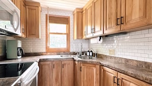 A kitchen with wooden cabinets, a built-in oven, a microwave, a sink, and a window. - The Darling Cabin, 60's Charm + Modern Flair (Alexandria)