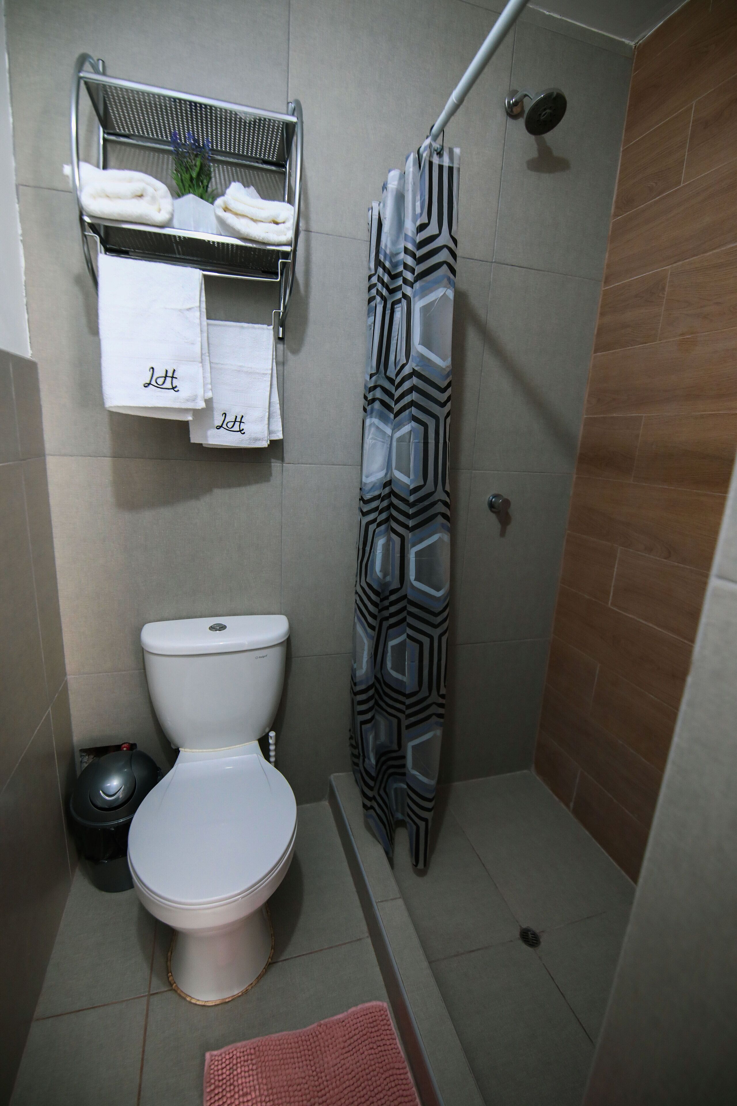 A compact bathroom with a toilet, a shower with a patterned curtain, and a towel rack with towels.
