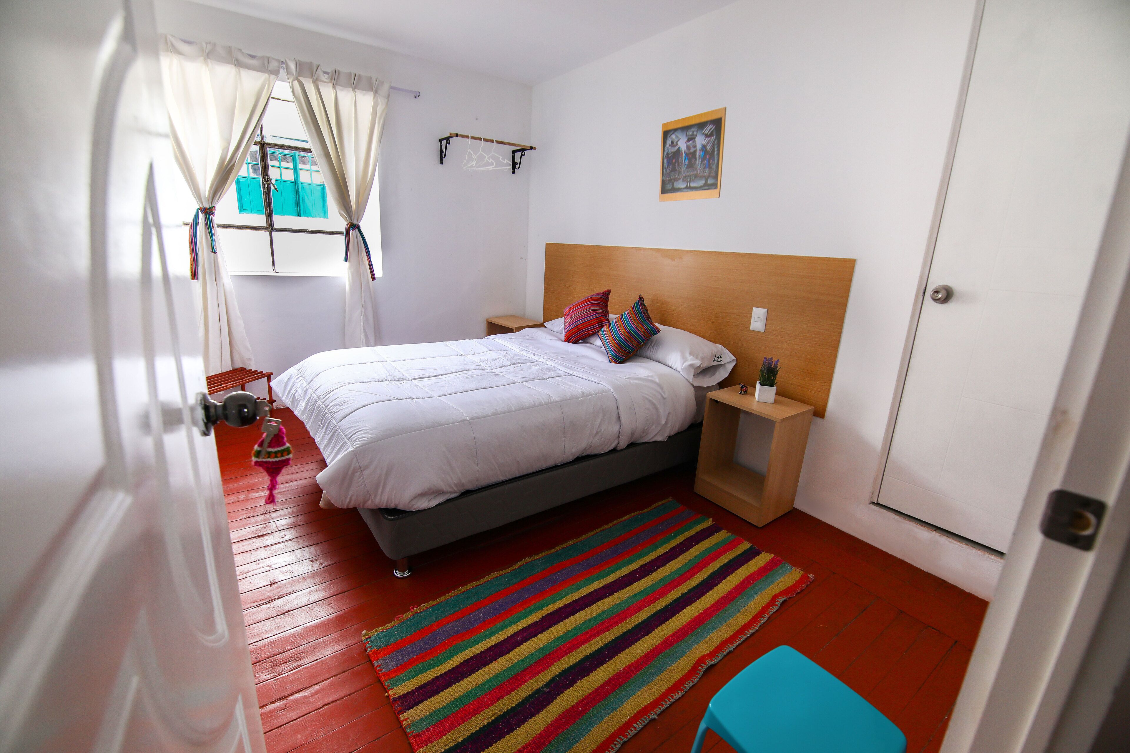 A bedroom with a bed, nightstands, a colorful rug, and a door.