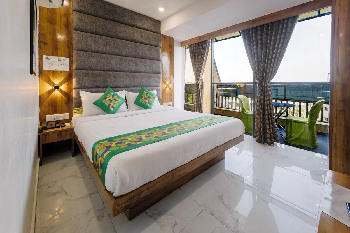 A hotel room with a large bed, a wooden headboard, a nightstand, and a balcony with a view.